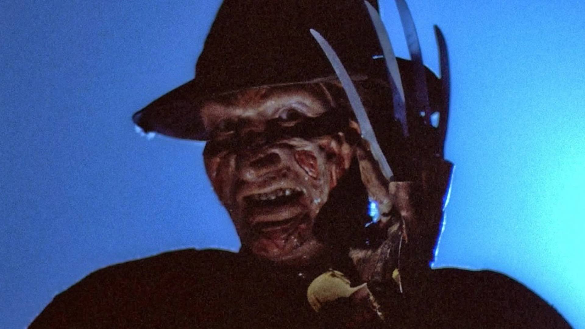 Freddy Krueger lit by a glowing blue background, raising his clawed glove.