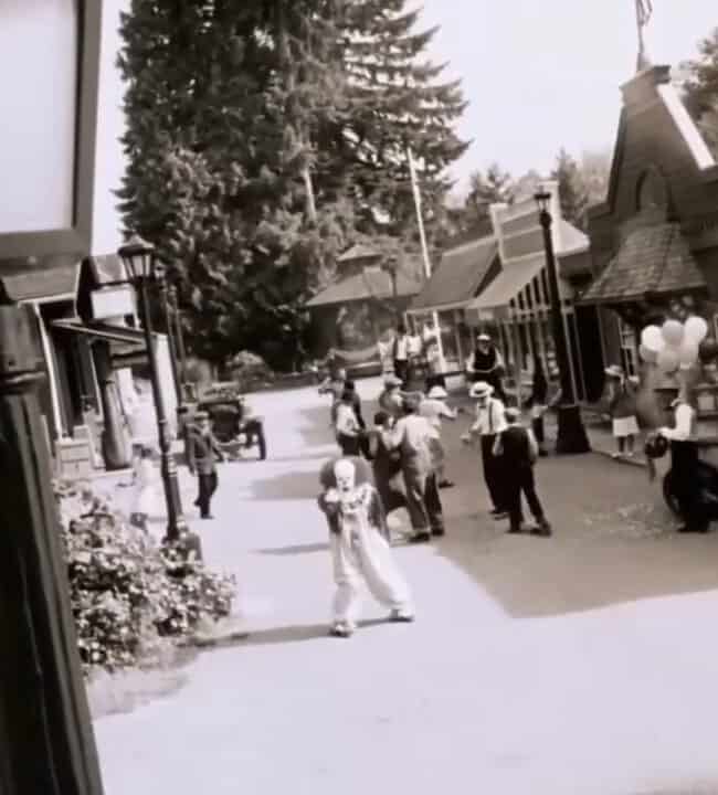 Black-and-white photo of a small-town street with families and shops.